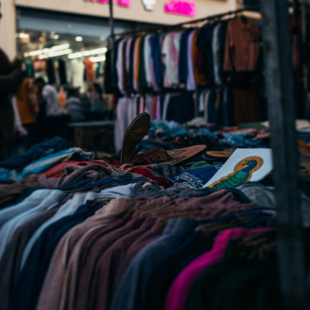 Ethical vs. Fast Fashion: What’s the Real Cost? Chaotic Delhi market stall with sandal, peacock patch.